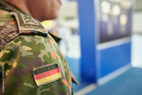 Bundeswehr Soldat in grüner Flecktarn Uniform und Flagge der Bundesrepublik Deutschland auf der rechten Schulter auf einem Informationsstand photo