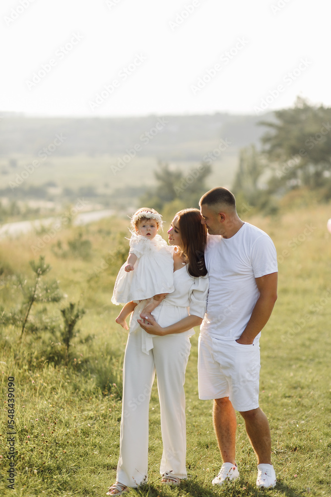Young family with cute little daughter walking in forest on the sunset