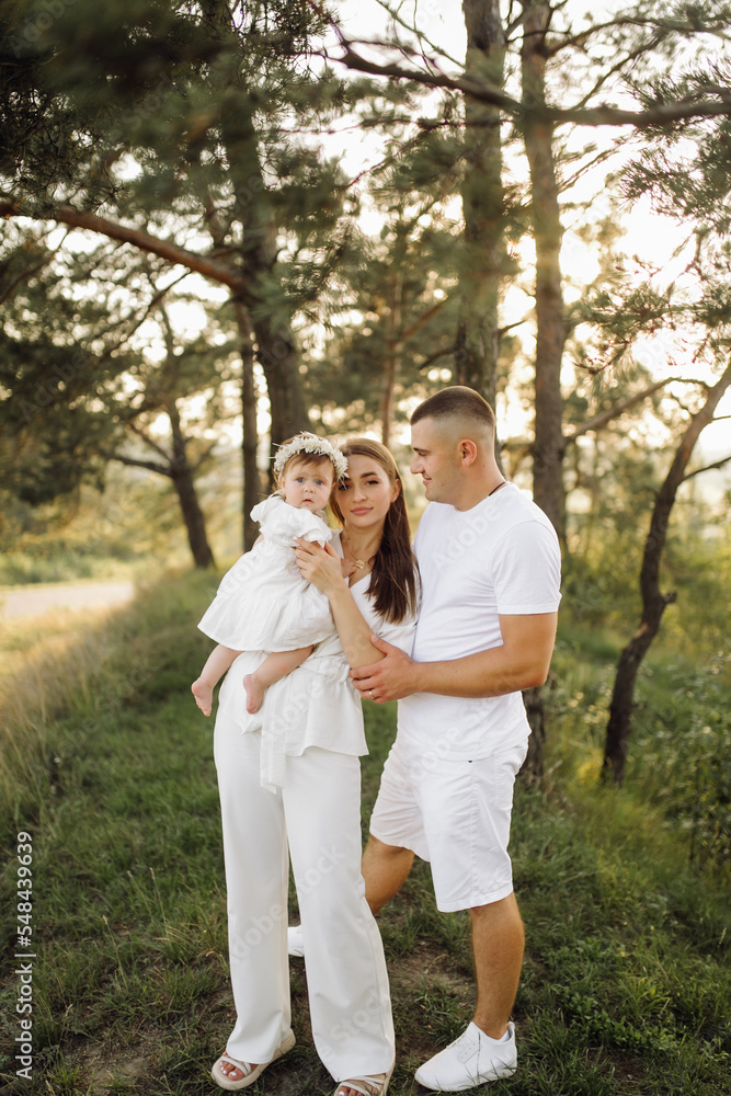 Fototapeta premium Young family with cute little daughter walking in forest on the sunset