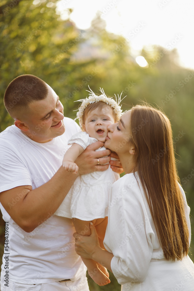 Fototapeta premium Young family with cute little daughter walking in forest on the sunset