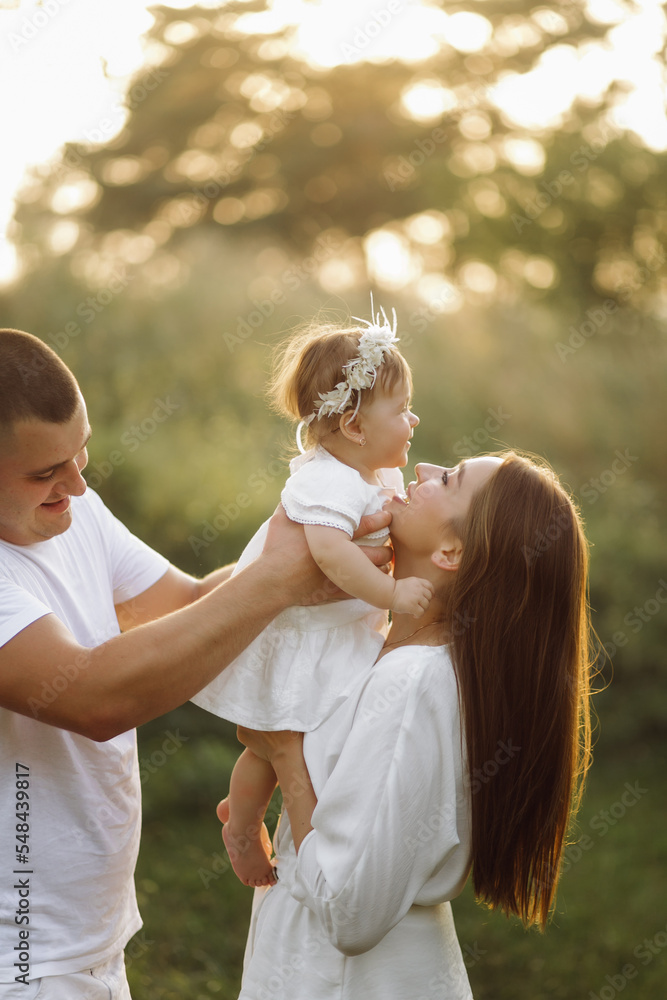 Fototapeta premium Young family with cute little daughter walking in forest on the sunset