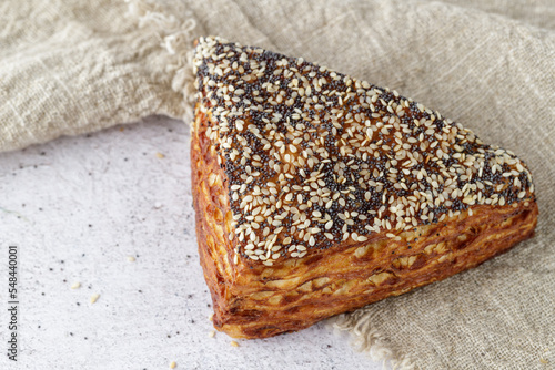 Fotografia Fresh baked puff lye corner with poppy and sesame seeds closeup on linen towel