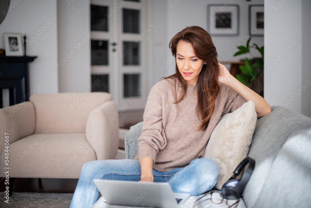 Attractive brunette haired woman using a laptop while working from home Attractive brunette haired woman using a laptop while working from home