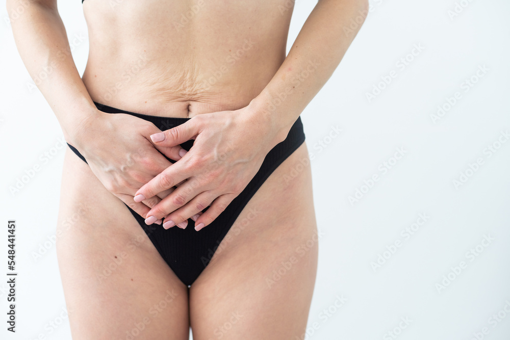 A woman in underwear holds her hands to her lower abdomen. Close-up. Beige background. The concept of gynecology and women's health