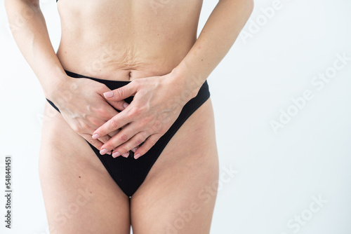 A woman in underwear holds her hands to her lower abdomen. Close-up. Beige background. The concept of gynecology and women s health