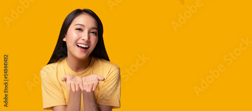Happy beautiful young asian woman stand over yellow background holding copy space imaginary on beauty palm for insert advertisement, happiness and smile face Smiling beautiful asia girl portrait © Nutlegal