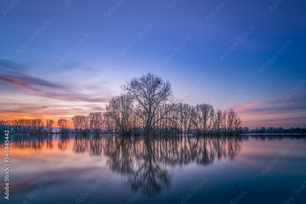 Sunset on the shore of a natural natural landscape lake in northern Europe. Reflections, blue sky and yellow sun. Landscape during sunset.