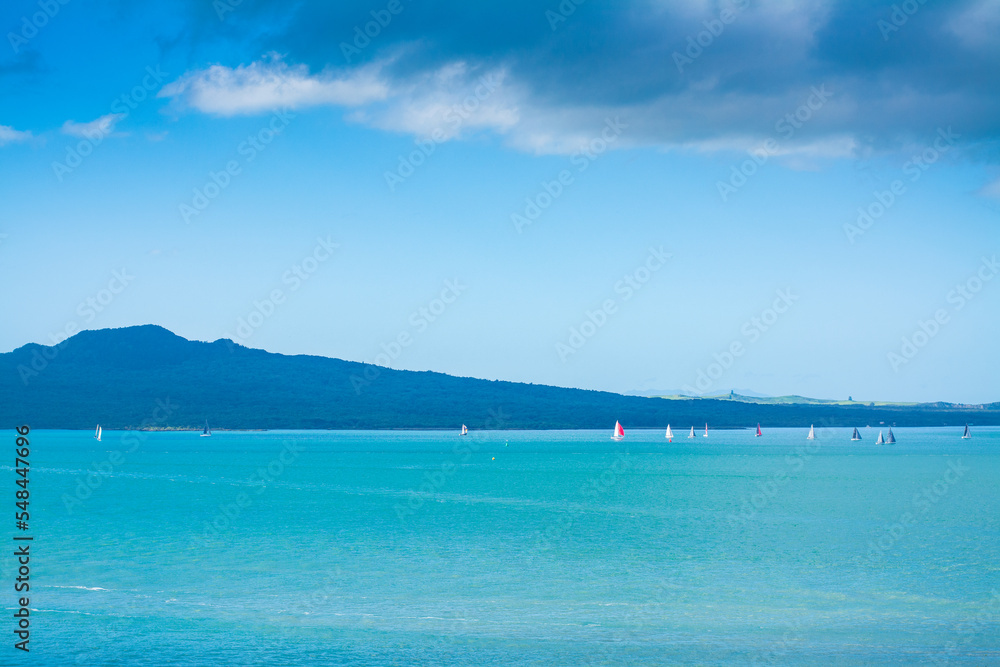 Small sailing boats scattered over calm waters of Auckland Harbour on a glorious winter day. Rangitoto Island seen on the horizon. North Island, New Zealand