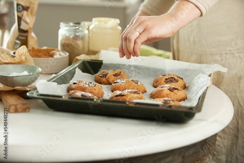 Closeup of female hands putting cookies on the black baking sheet pouring on ingredients around