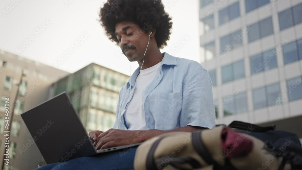 Young African American man with afro hairstyle and moustache, talking on online video call using laptop outside the office Young African American man with afro hairstyle and moustache, talking on online video call using laptop outside the office