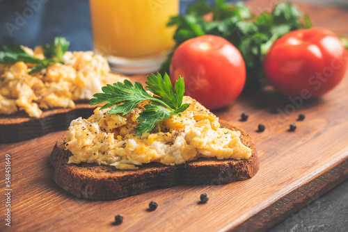 Scrambled eggs with parsley on bread, homemade healthy breakfast on dark wooden board