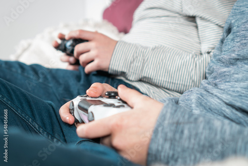 Cropped photo of two teenage boys children sitting at home, holding gaming controller joystick gamepad, playing videogames. Hobby, free time, gaming, entertainment, leisure, friendship. Soft focus.