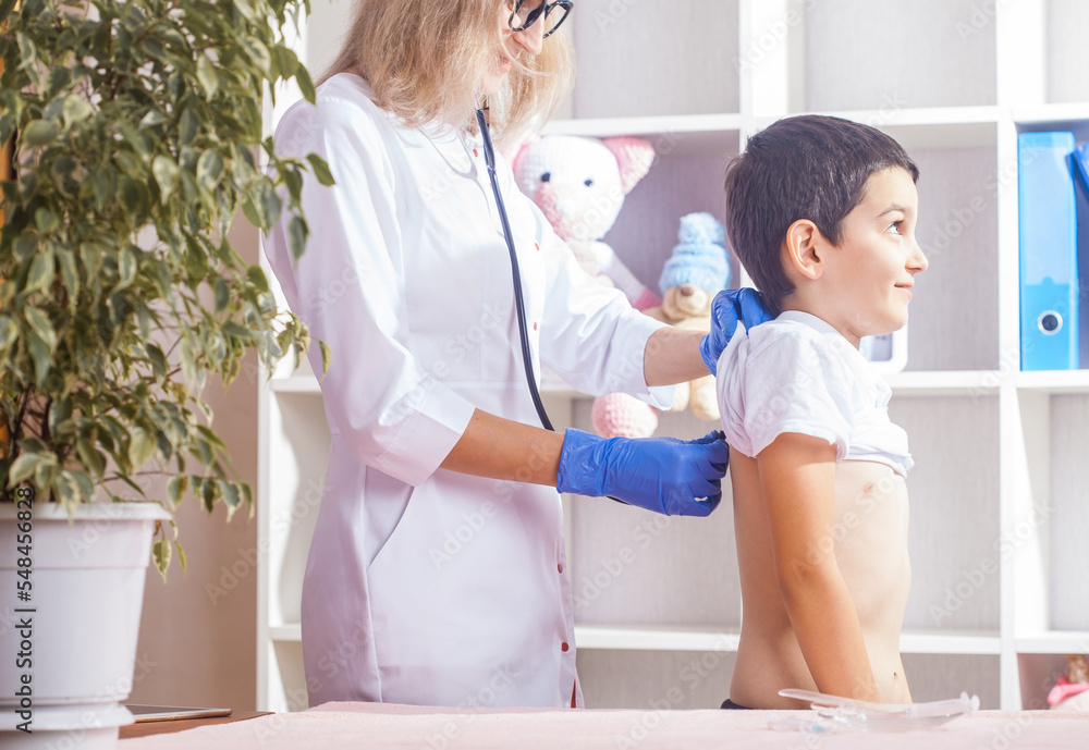 Fototapeta premium pediatrician with stethoscope listening to heartbeat boy's patient on medical exam at clinic. kid boy on medical examination checkup