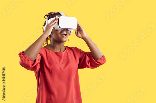 Smiling African American woman enjoy vision in vr glasses isolated on yellow studio background. Happy excited black wear virtual reality headset explore new horizons. Technology concept.