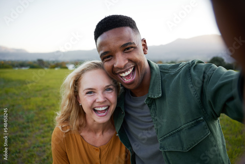 Young multiracial couple in casual clothing laughing and looking at camera in field