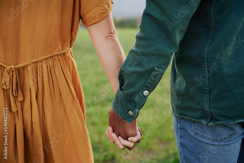 Close-up of multiracial young couple in casual clothing holding hands in field