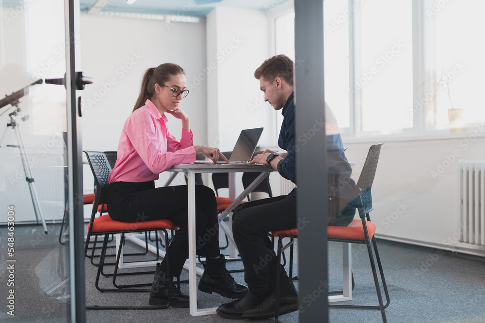 Two young entrepreneurs, a businessman and a businesswoman, sitting in a modern glass office and exchange business ideas Two young entrepreneurs, a businessman and a businesswoman, sitting in a modern glass office and exchange business ideas