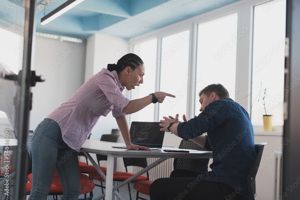 Emotional couple of young colleagues arguing in modern office. African-american business woman shouting at her sad man assistant, copy space, side view Emotional couple of young colleagues arguing in modern office. African-american business woman shouting at her sad man assistant, copy space, side view