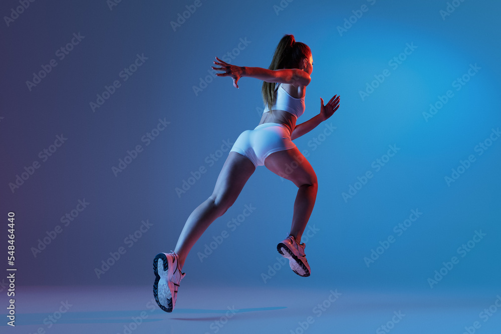 Young sportive girl in white sportswear training isolated over gradient blue purple studio background in neon light. Run