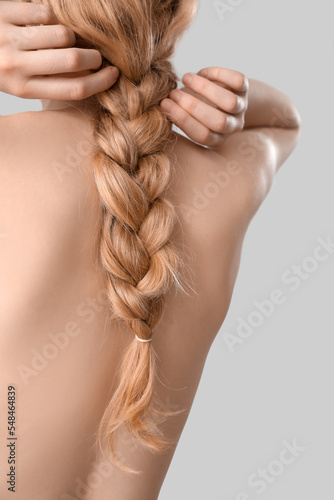 Blonde woman with naked back adjusting pigtail hairstyle on light background photo