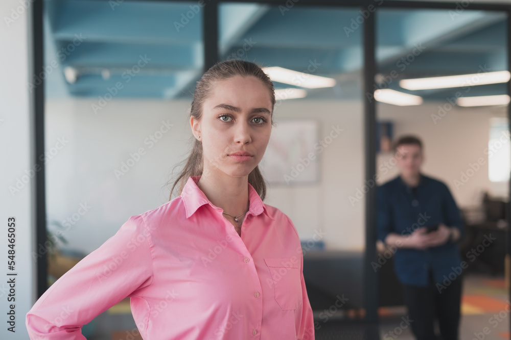 Obraz premium Portrait of young smiling business woman in creative open space coworking startup office. Successful businesswoman standing in office with copyspace. Coworkers working in background.