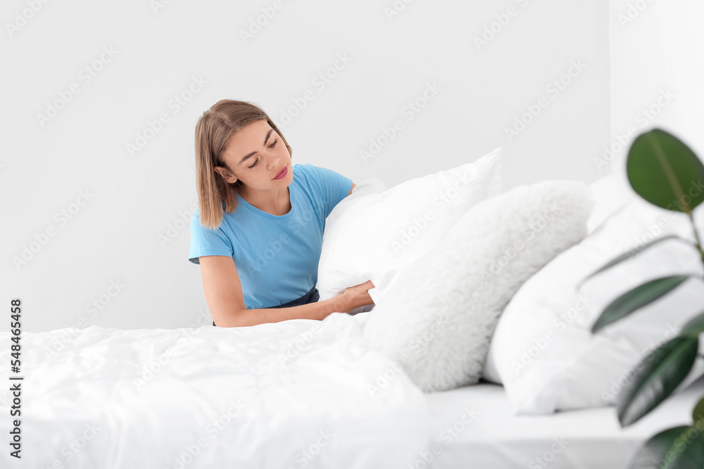 Young housewife adjusting pillow in bedroom Young housewife adjusting pillow in bedroom