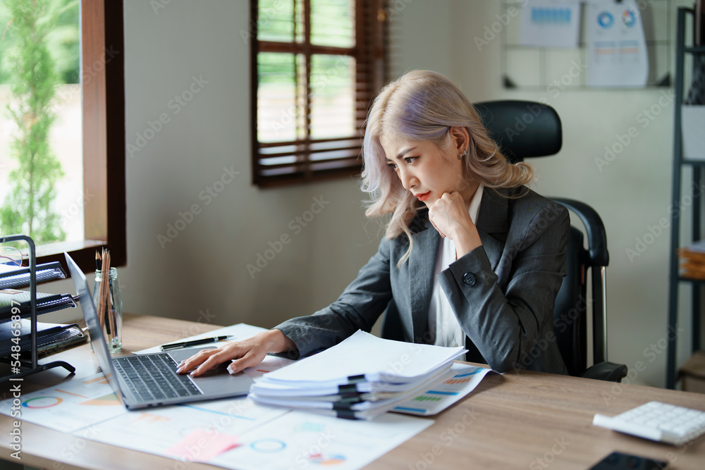 Portrait of a thoughtful Asian businesswoman looking at financial statements and making marketing plans using a computer on her desk Portrait of a thoughtful Asian businesswoman looking at financial statements and making marketing plans using a computer on her desk