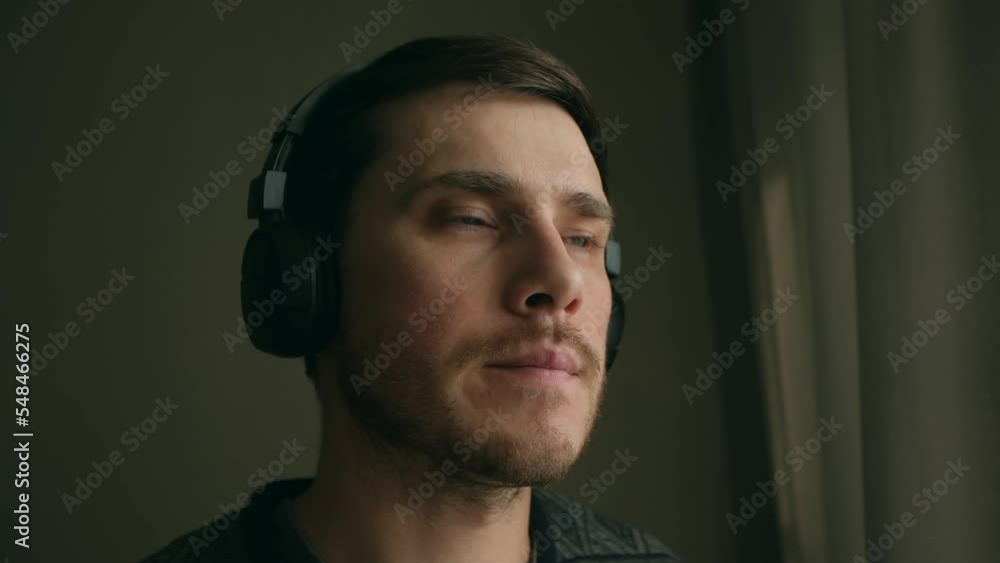 close up portrait young man puts on headphones enjoying listening to music near window at the morning or day close up portrait young man puts on headphones enjoying listening to music near window at the morning or day