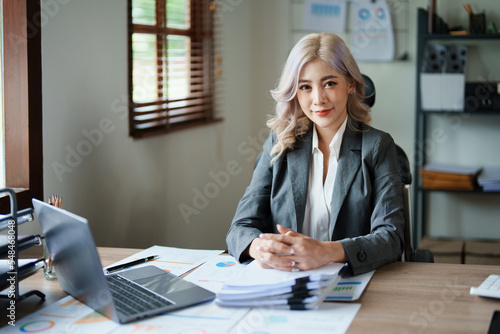Portrait of a woman business owner showing a happy smiling face as he has successfully invested her business using computers and financial budget documents at work