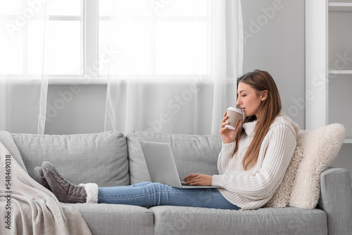 Young woman with cup of coffee using laptop at home