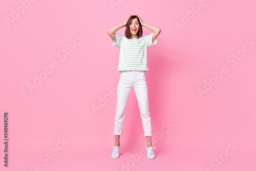 Full length photo of optimistic impressed girl wear striped t-shirt white pants shoes arms on head yell isolated on pink color background