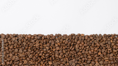Coffee beans laid out in one wide row on a white background, place for inscription and advertising. © Niko_Dali