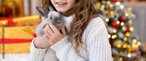 Cute Christmas bunny Symbol of the New year 2022 close-up in the hands of a child on the background of a decorated Christmas tree with defocus lights