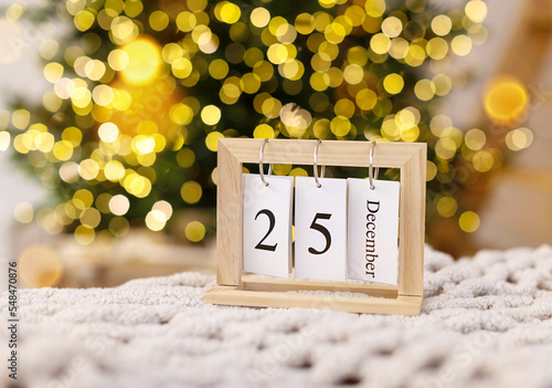 Wooden christmas calendar date 25 december on the background of a decorated Christmas tree with defocus lights