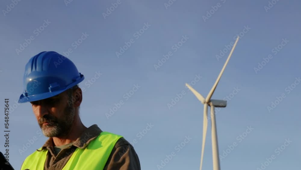 Castilla y León, Spain. October 13, 2022. Male renewable energy engineer, from behind checking wind tower. He turns to camera Castilla y León, Spain. October 13, 2022. Male renewable energy engineer, from behind checking wind tower. He turns to camera
