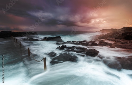 Stormy weather and large swell waves wash over rocks into rock pool