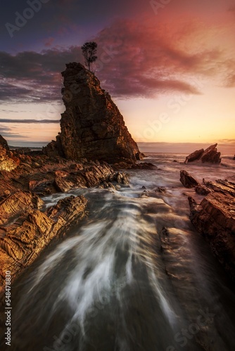 Water flowing fast through narrow chasm beside seastack woth sol