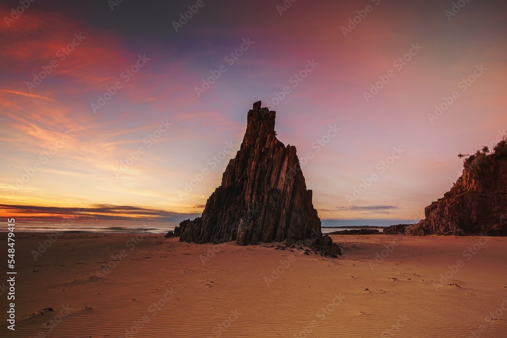 Pyramid sea stack on beach with beautiful sunrise sky with red clouds