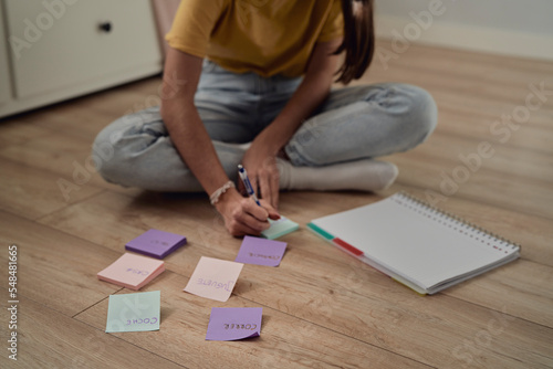 Unrecognizable caucasian teenage girl sitting on floor and making notes on flash cards