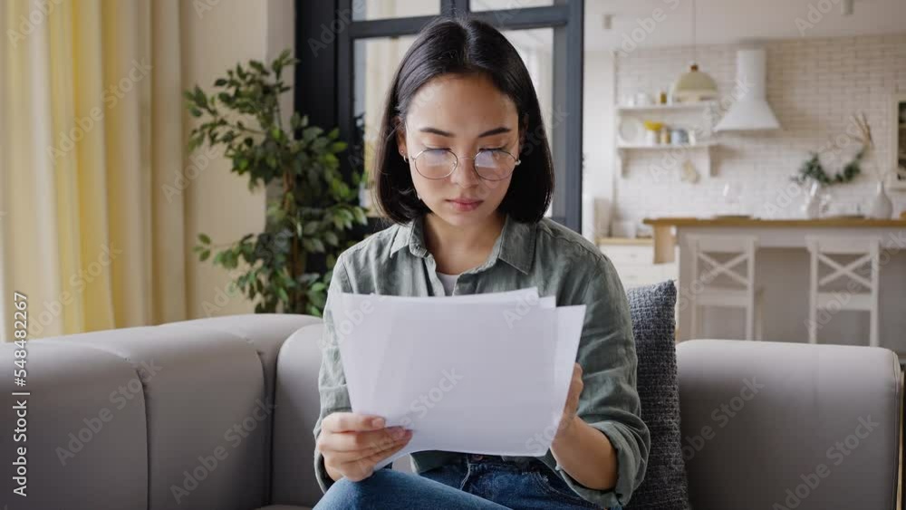 Young Asian woman reads paper documents attentively Young Asian woman reads paper documents attentively