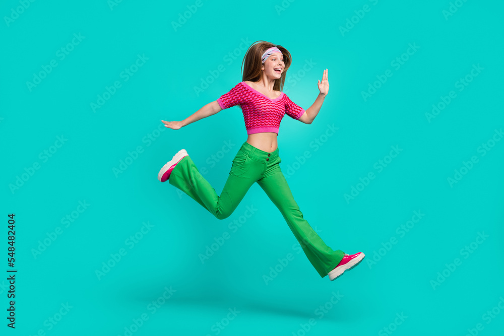 Full length photo of sweet impressed schoolgirl wear pink crop top flare trousers jumping high isolated turquoise color background