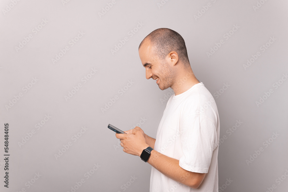 Side view photo of young man in white t-shirt using mobile phone over grey background Side view photo of young man in white t-shirt using mobile phone over grey background