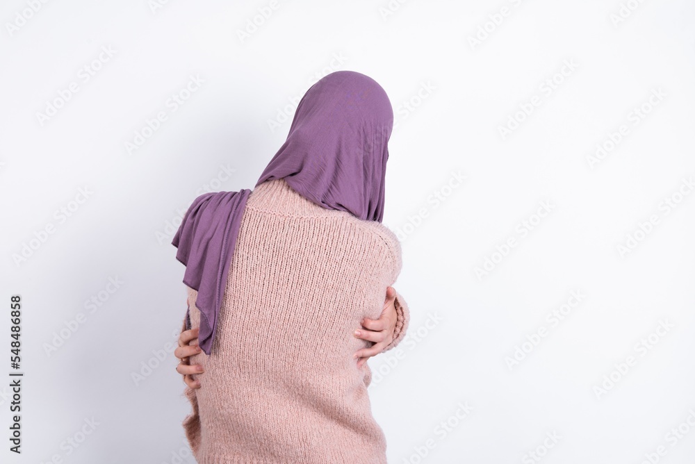 Φωτογραφία muslim woman wearing hijab and knitted sweater over white background hugging herself happy and positive from backwards