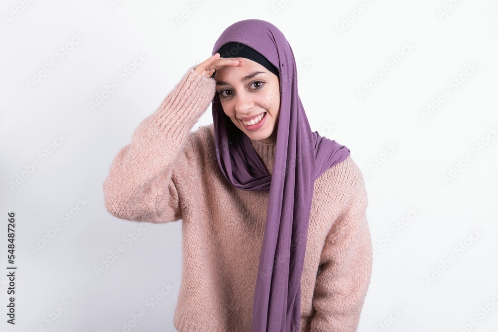 Φωτογραφία beautiful muslim woman wearing hijab and warm jumper over white background very happy and smiling looking far away with hand over head