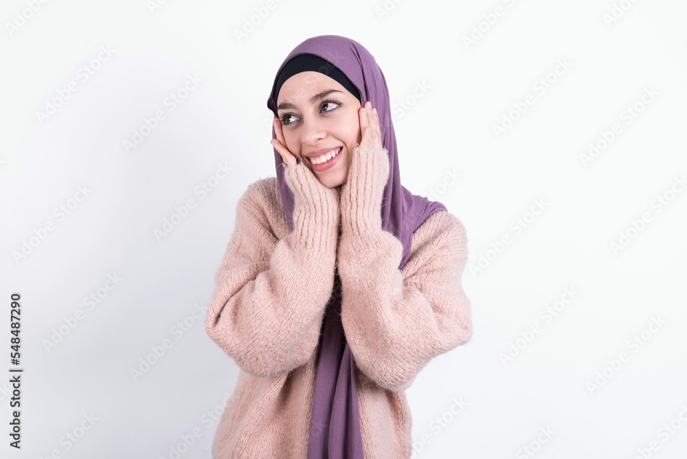 Inspired beautiful muslim woman wearing hijab and warm jumper over white background looking at copyspace having thoughts about future events Inspired beautiful muslim woman wearing hijab and warm jumper over white background looking at copyspace having thoughts about future events