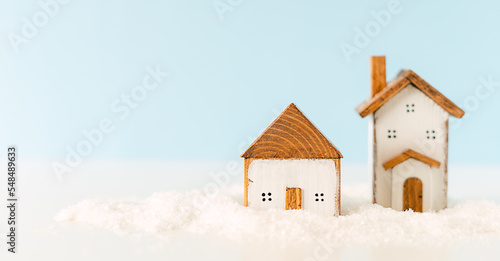 Happy New Year and Merry Christmas banner. Festive blue background with toy wooden house, snow, rustic Christmas village and decoration. Copy space for winter holidays greeting card. 
