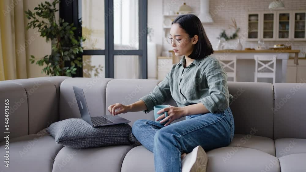 Smiling Asian woman works on laptop drinking hot beverage Smiling Asian woman works on laptop drinking hot beverage