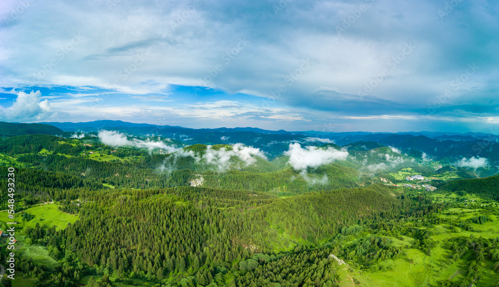 Fototapeta premium Valley of Balkan mountains with fog, sunny clouds and forests. Village Pamporovo. Panorama, top view