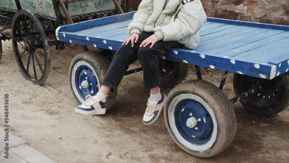 Playful teenage girl dangling legs while relaxing on cart. Female is wearing jacket while traveling. She is spending leisure time during vacation Playful teenage girl dangling legs while relaxing on cart. Female is wearing jacket while traveling. She is spending leisure time during vacation
