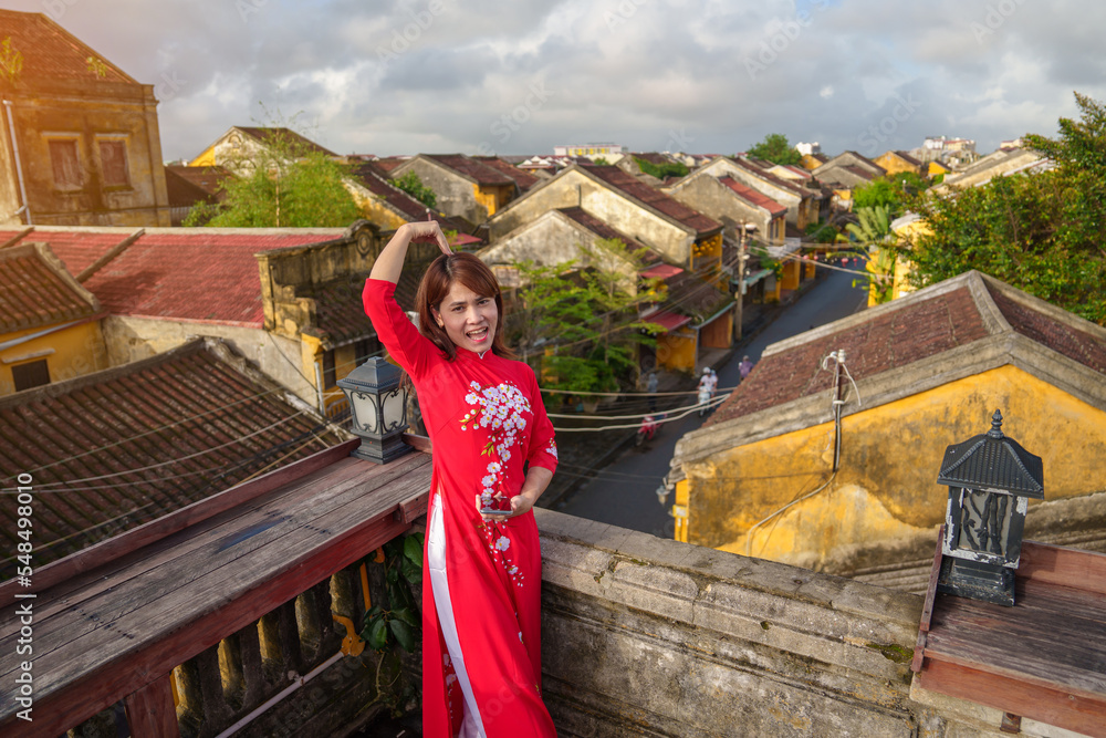 happy woman wearing Ao Dai Vietnamese dress, traveler sightseeing view at rooftop at Hoi An ancient town in Vietnam. landmark and popular for tourist attractions. Vietnam and Southeast travel concept